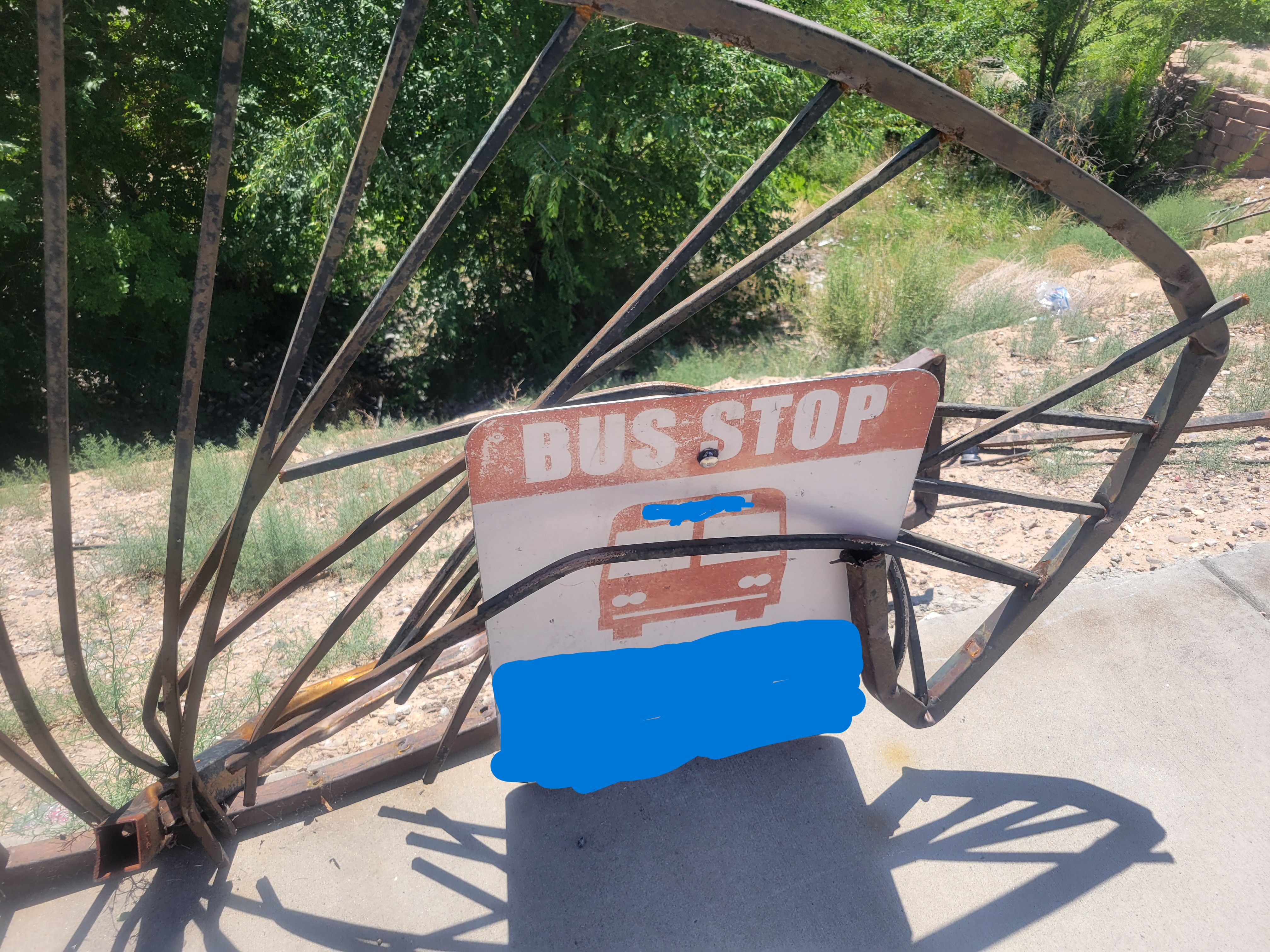 Warped rusted fence with bus stop sign in it.